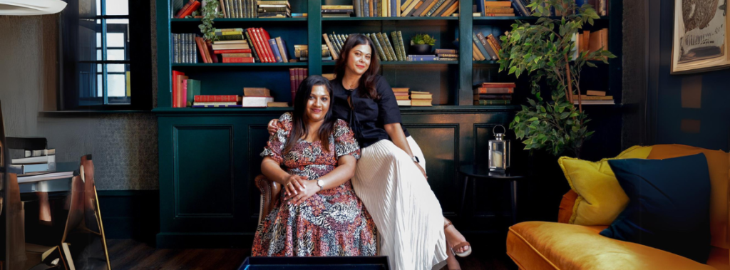 Two women sitting on a chair in a library| Lets Pour and Ponder Podcast : Girly podcast | Woman podcast| Podcast for women