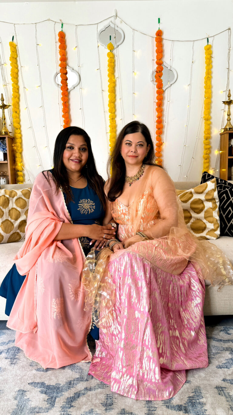 Two indian women sitting on a sofa all decked up in indian clothes for diwali. Podcast hosts| Lets pour and ponder